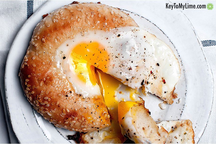 Egg in a hole bagel on a plate with runny yolk and a bite missing.