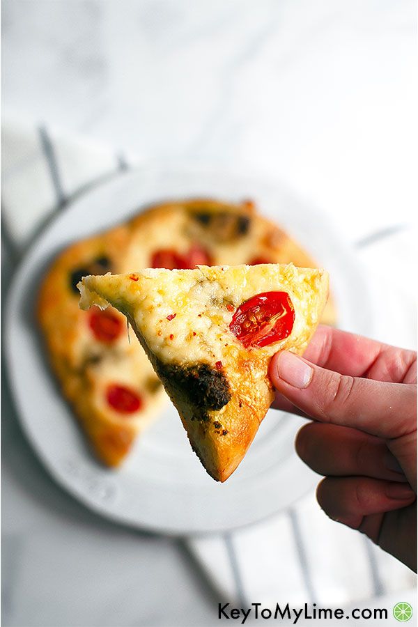 A hand holding a slice of pesto pizza.