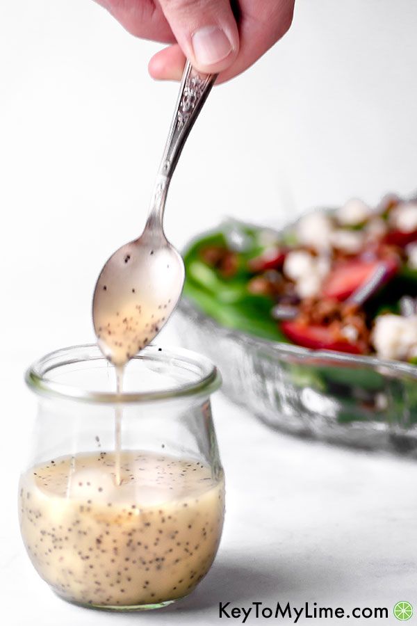 A spoon lifting poppy seed dressing out of a jar with a salad in the background.