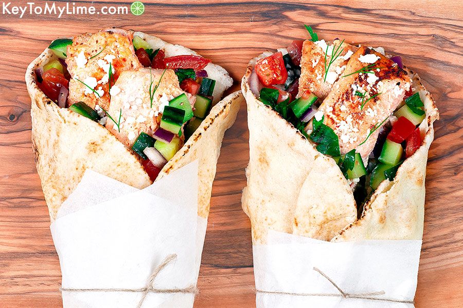 An overhead image of two salmon gyros on a wood cutting board wrapped in parchment paper.