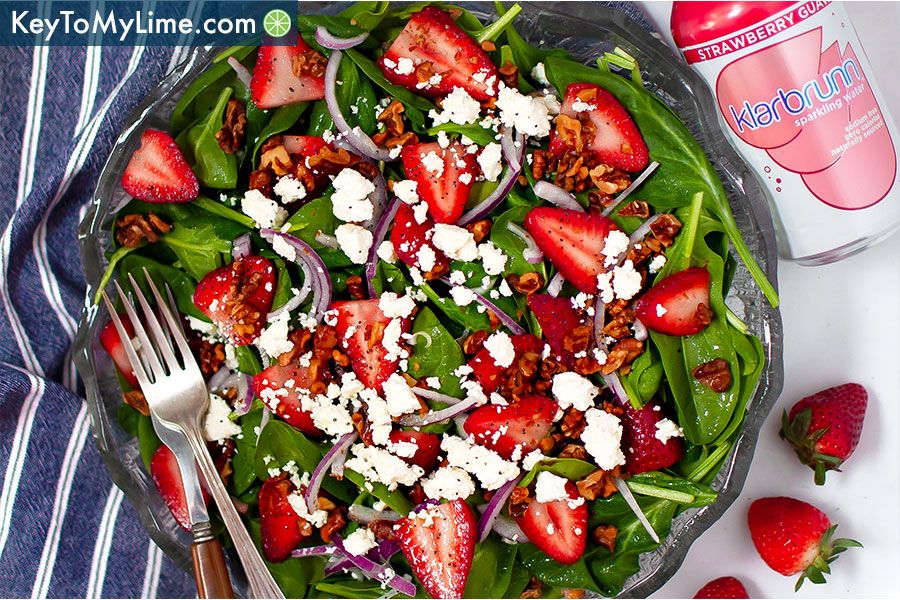 An overhead image of strawberry spinach salad with a fork and knife on a blue striped napkin.
