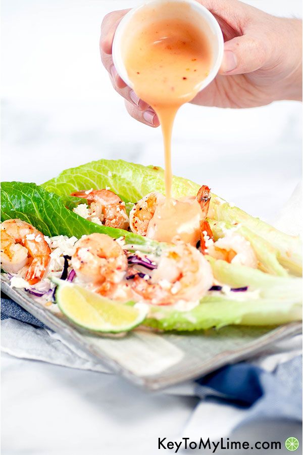 A hand pouring bang bang sauce on shrimp lettuce cups.