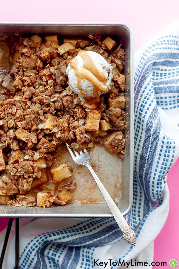 Apple crisp with a scoop of ice cream and a fork on a pink background.