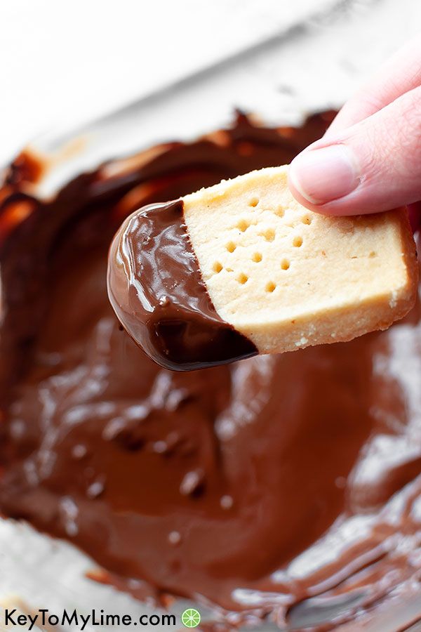 A keto shortbread cookie being dipped in melted chocolate.