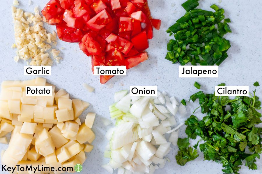 Garlic, tomatoes, jalapeno, potato, onion, and cilantro in labeled piles on a cutting board.