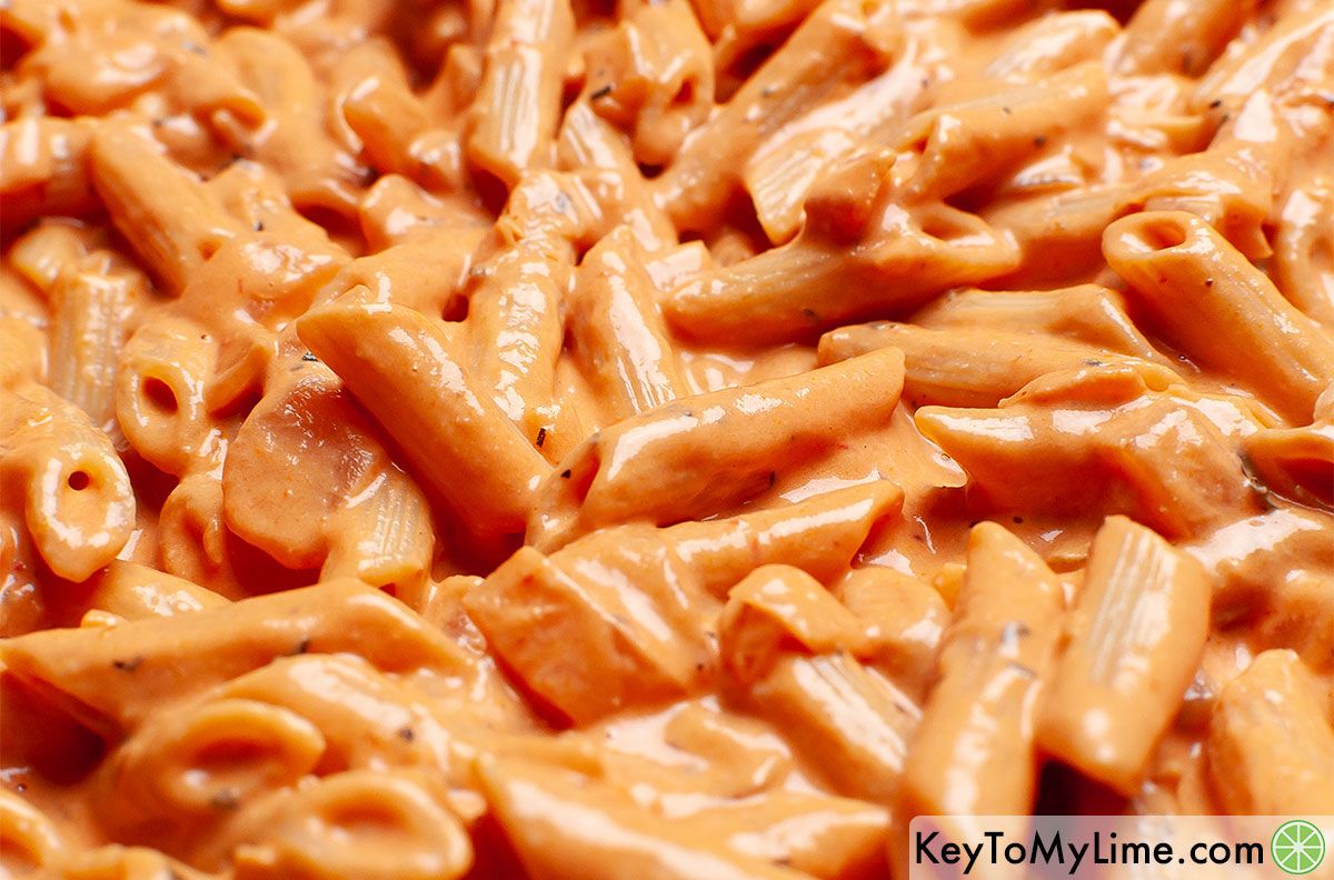 A close up image of penne noodles tossed in creamy tomato sauce.