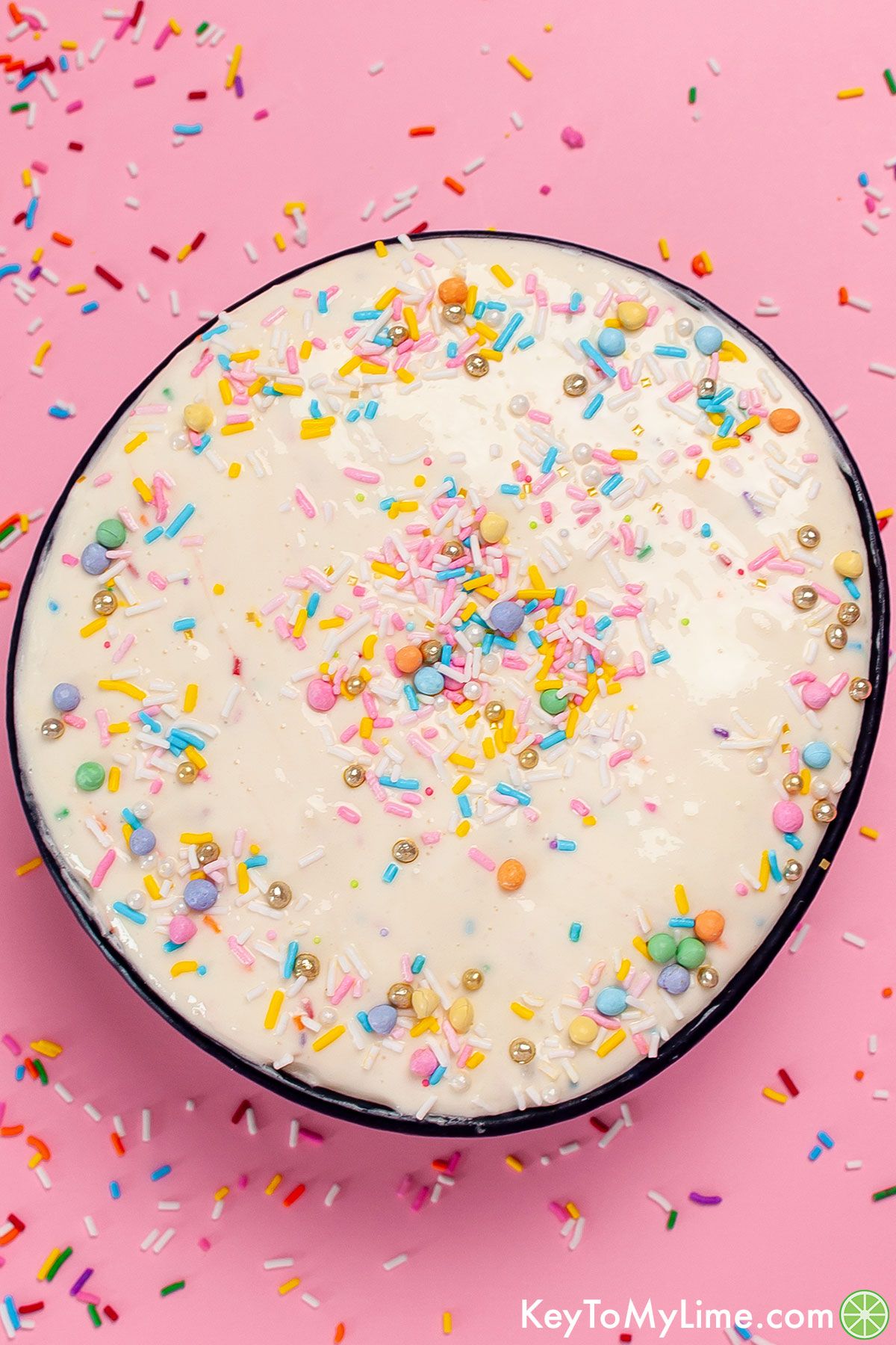 A bowl of funfetti dip against a pink background with sprinkles spread around.