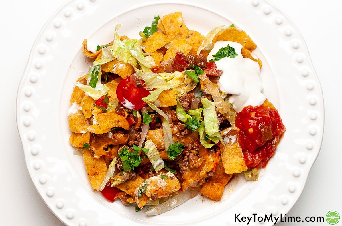 A serving of walking taco casserole on a plate with dollops of salsa and sour cream.