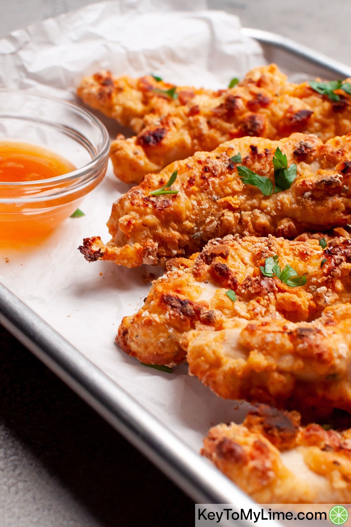 Chicken tenders on a small baking sheet next to a container of plum sauce.