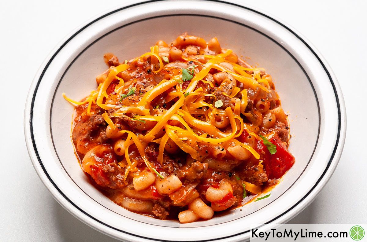 A bowl of American goulash topped with shredded cheddar cheese.