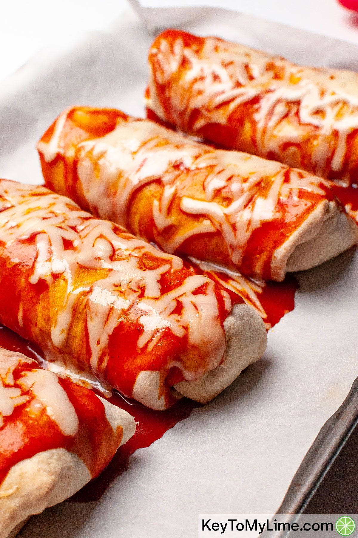 A side image of four wet burritos on a baking sheet.