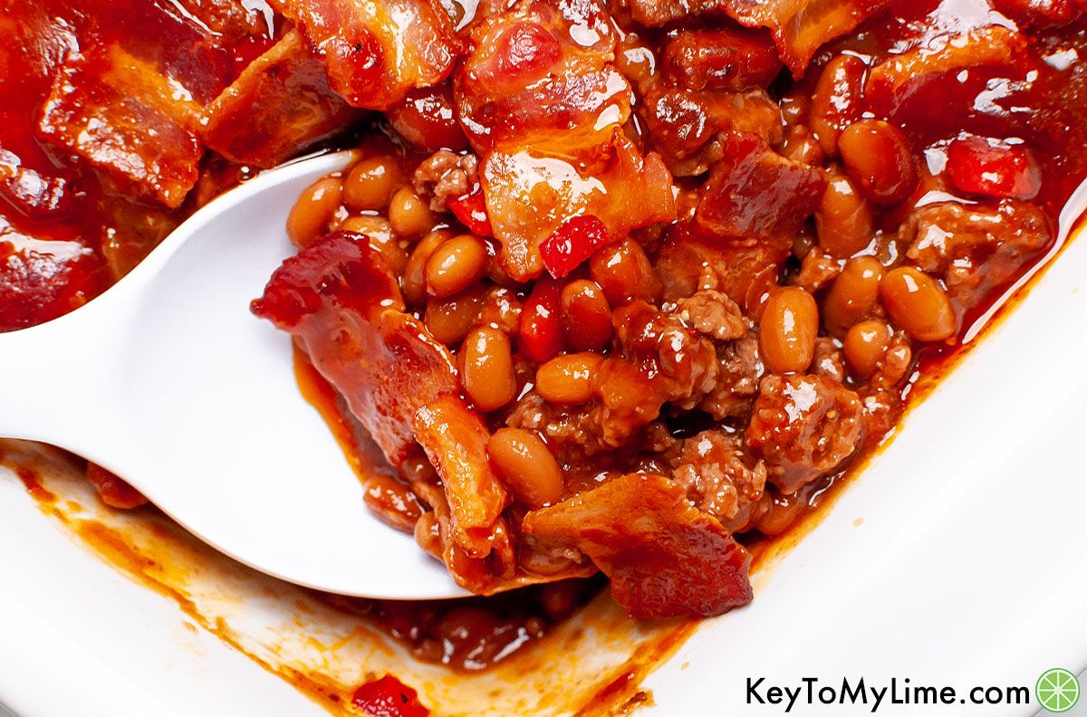 A spoon scooping out a serving of baked beans with ground beef.