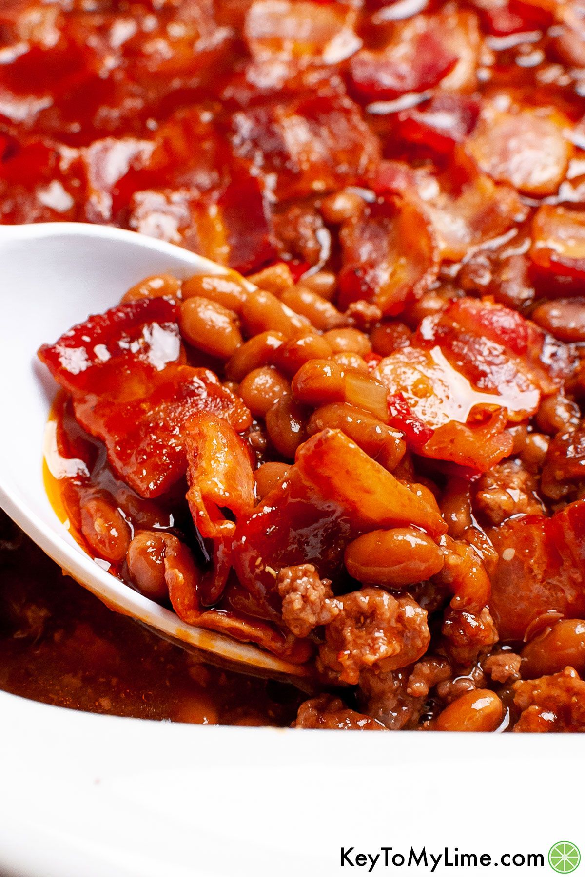 A serving spoon scooping out a portion of baked beans from the casserole dish.