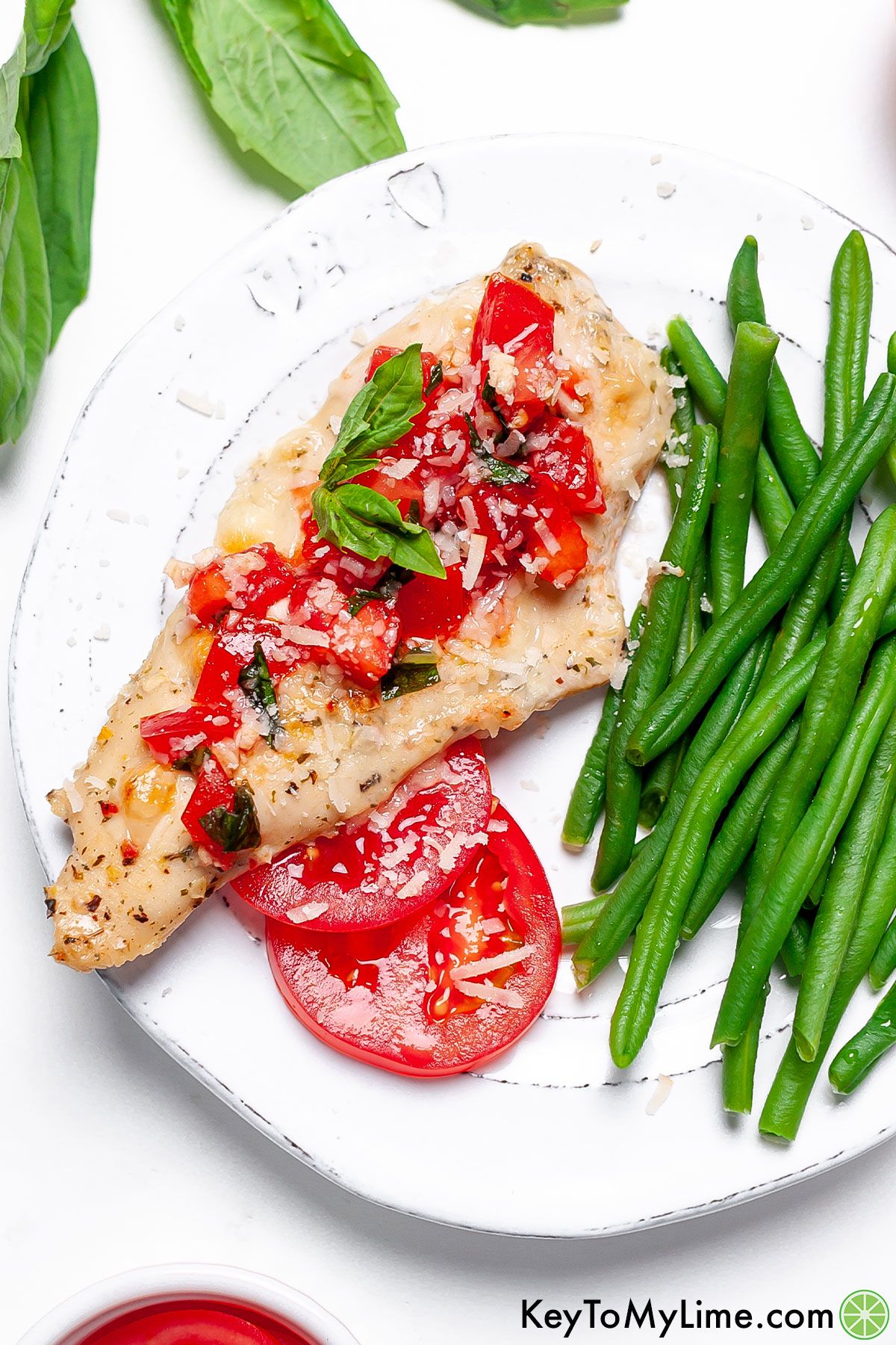 Bruschetta chicken with tomato slices, fresh basil, and green beans.
