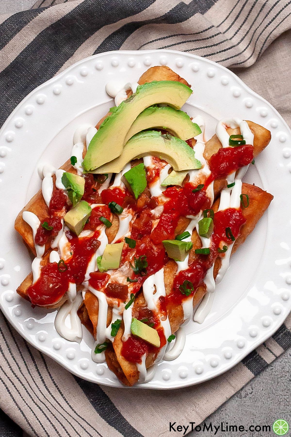Chicken flautas topped with salsa, sour cream, and avocado.