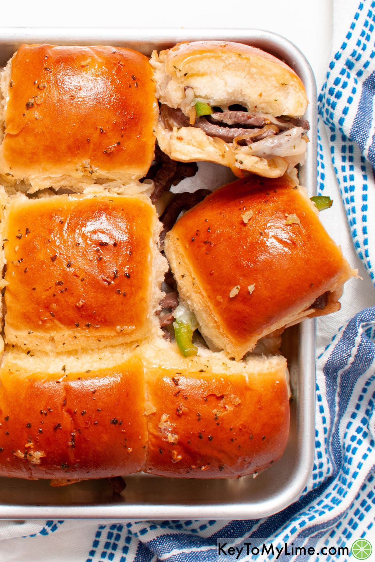 A tray of Philly cheesesteak sliders photographed on a blue striped napkin.