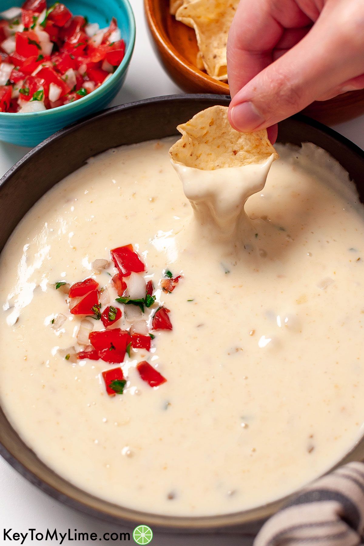 A tortilla chip scooping up white queso dip to show how stretchy it is.