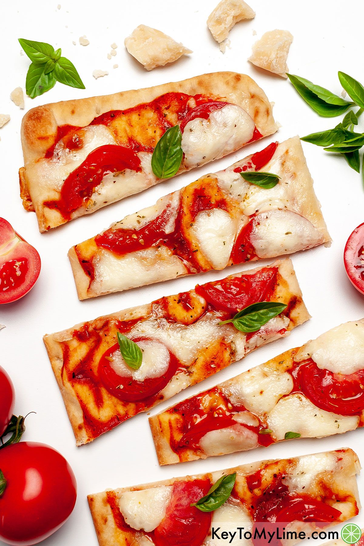 Sliced margherita flatbread surrounded by tomatoes and basil.