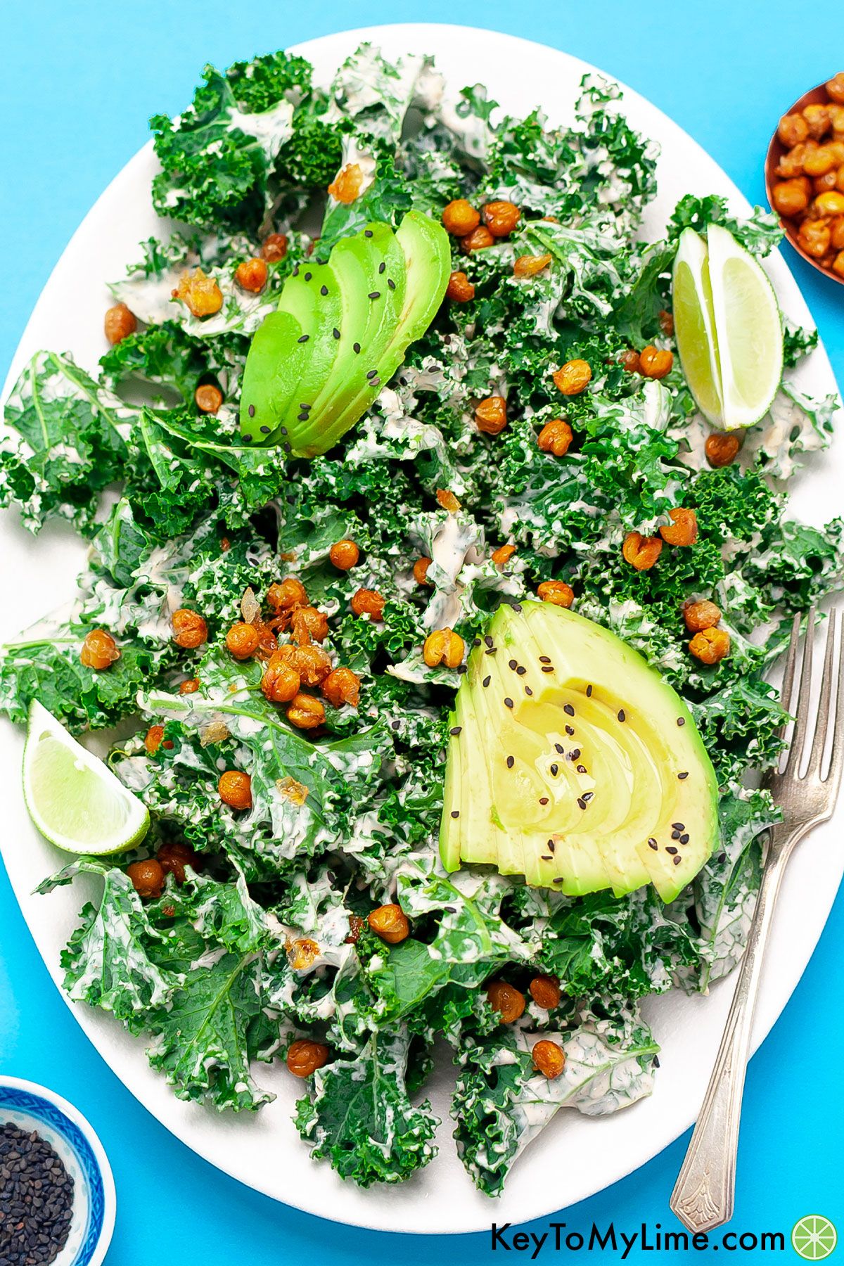 A kale and avocado salad on a white platter against a blue background.