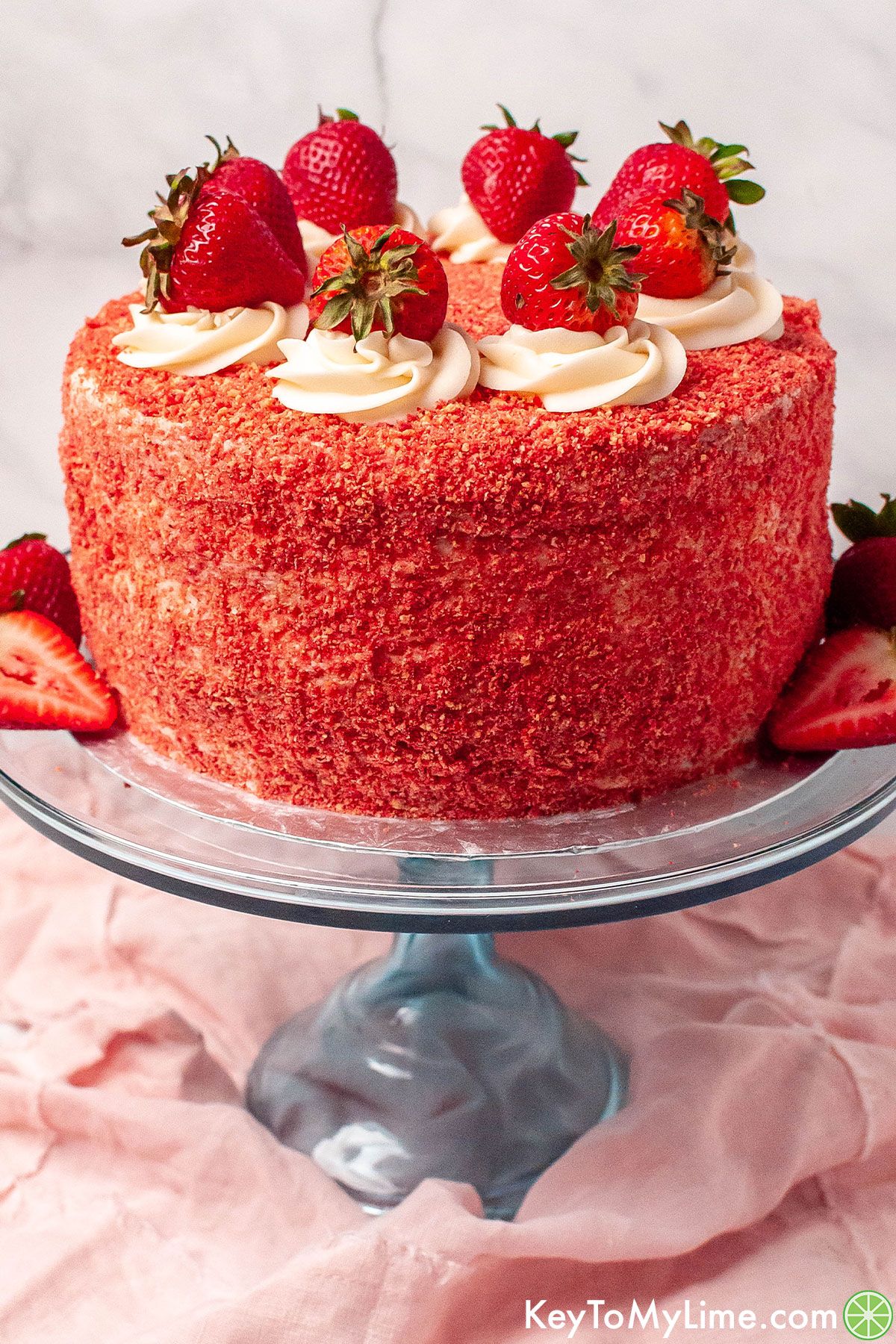 A decorated strawberry crunch cake on a blue glass cake stand.