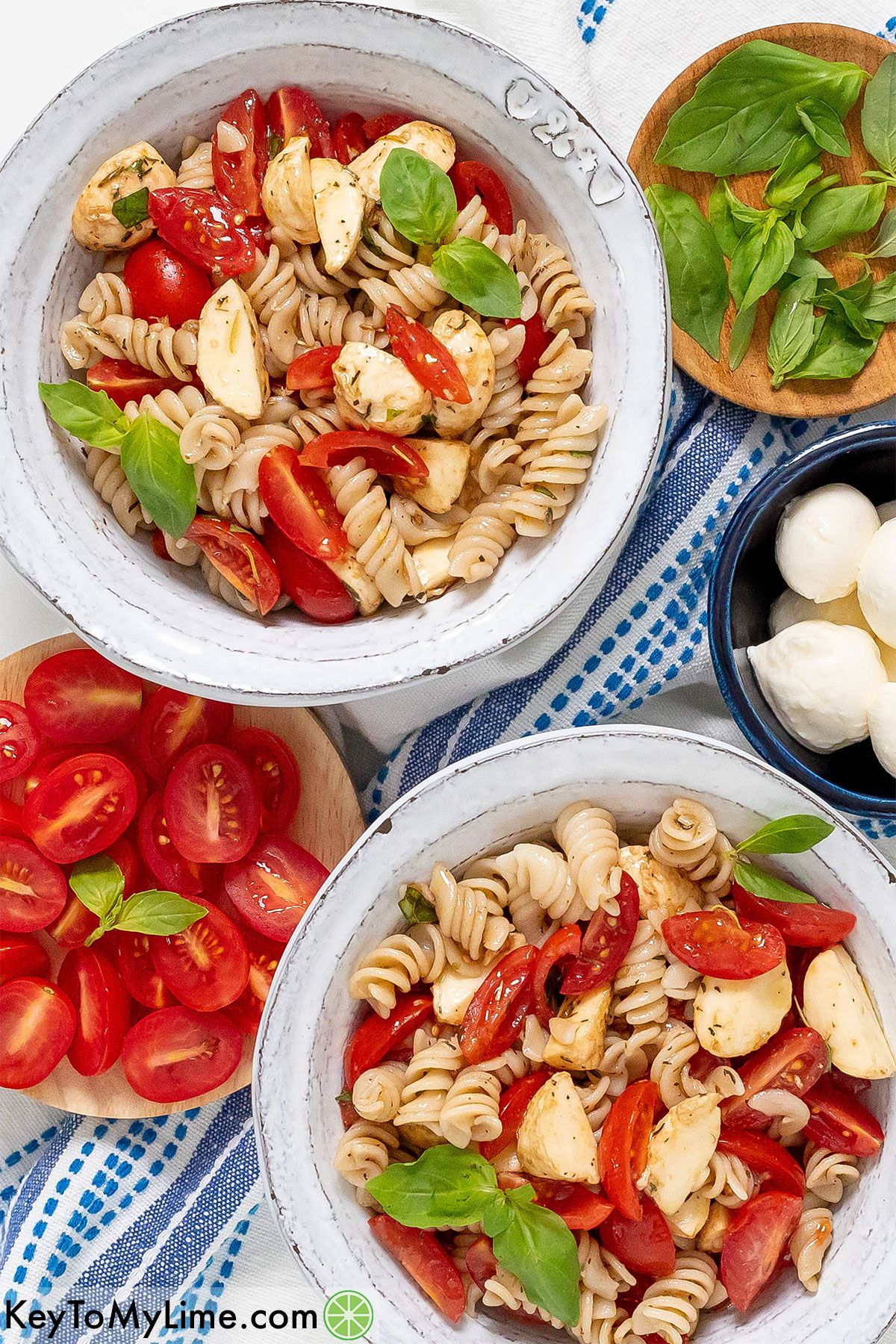 Two bowls of caprese pasta salad on a blue and white napkin.