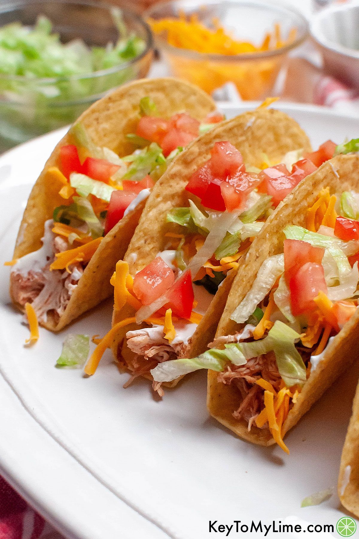 A close up of hard shell tacos filled with shredded salsa chicken.