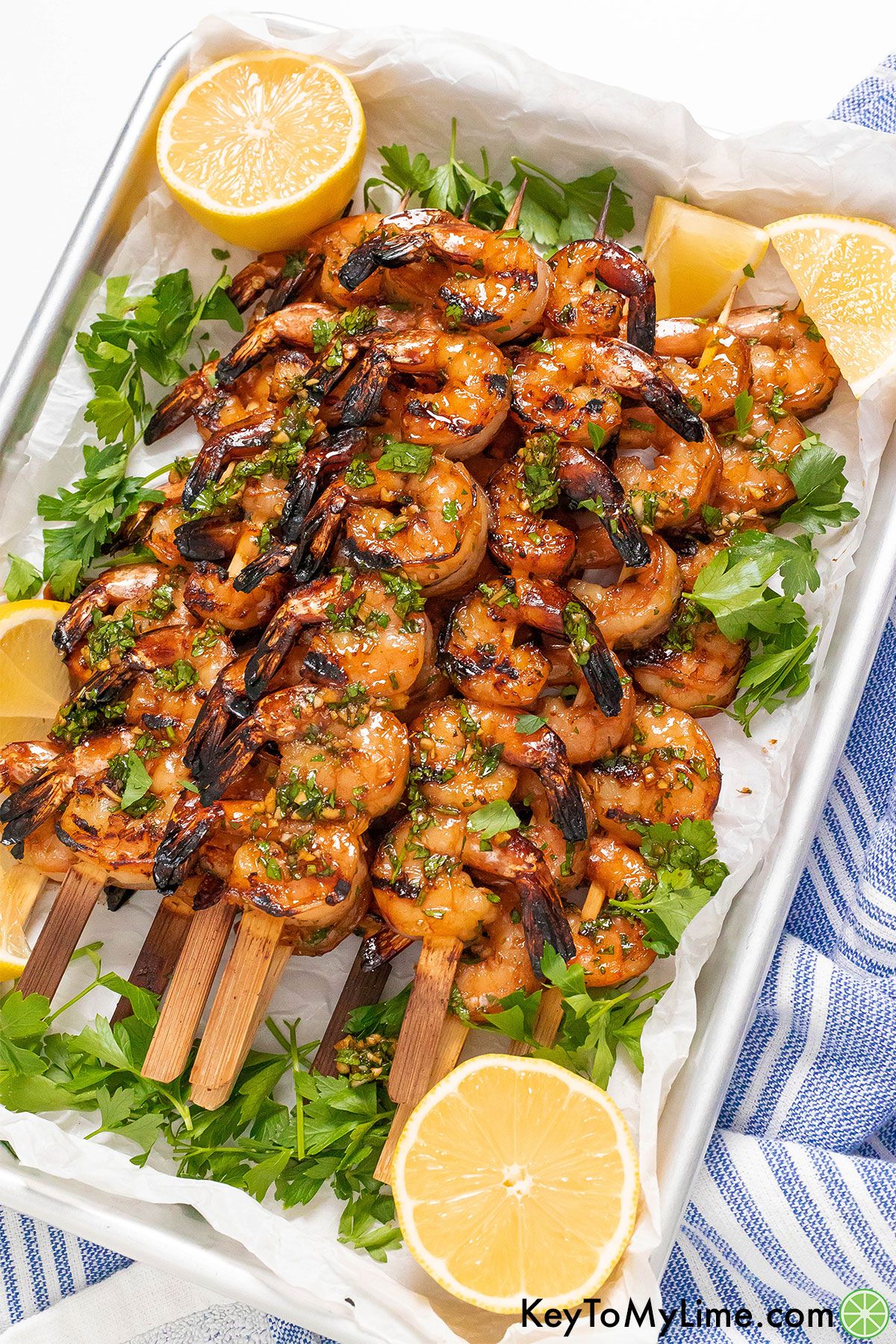 A platter of grilled shrimp kabobs on top of a blue striped napkin.