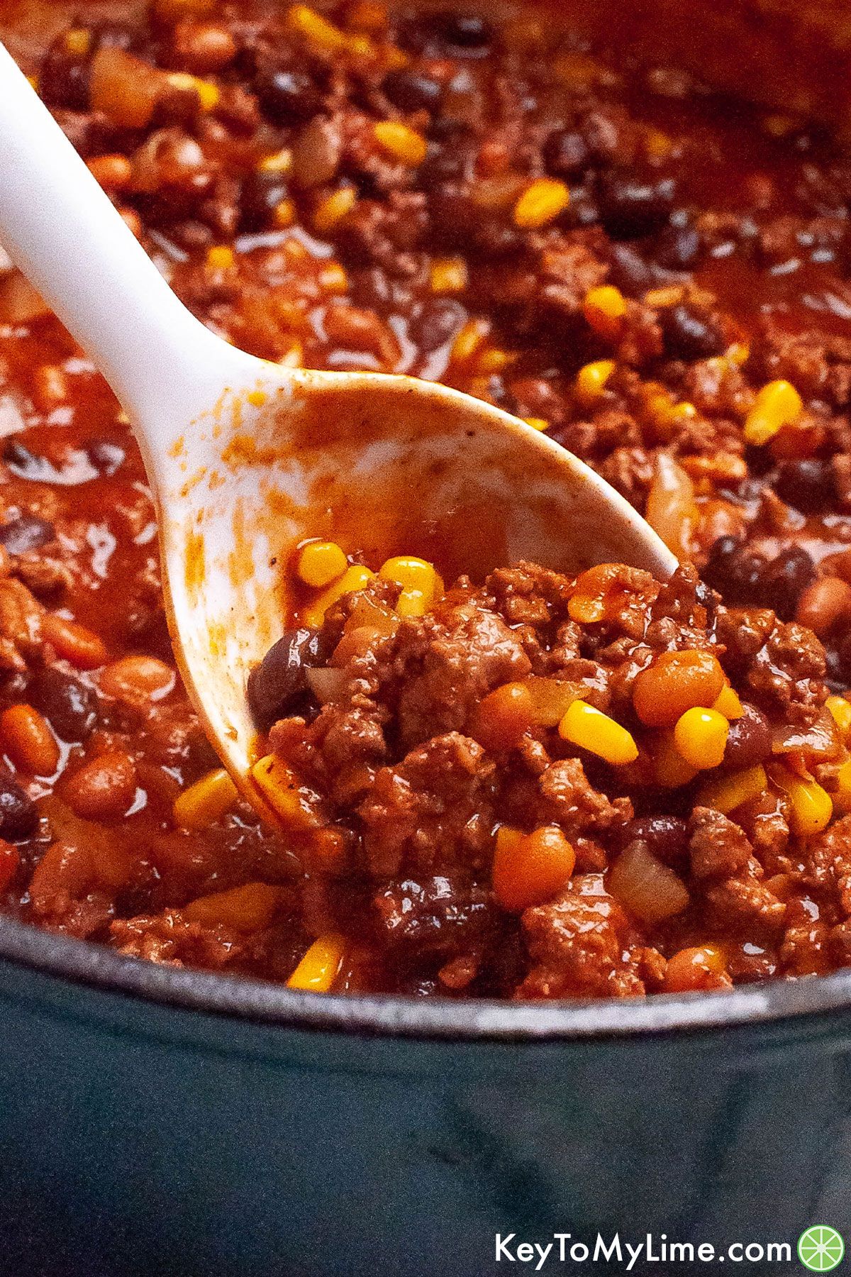 A white serving spoon scooping out a serving of sweet chili.