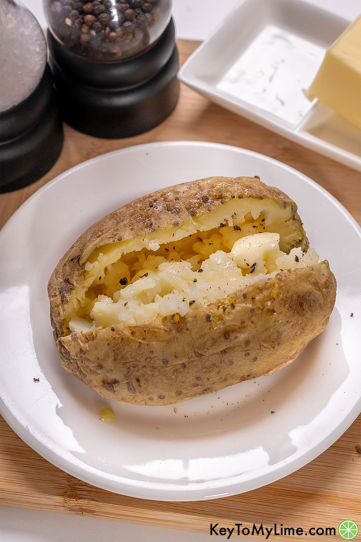 A close up image of a freshly cooked potato served with butter salt and pepper.
