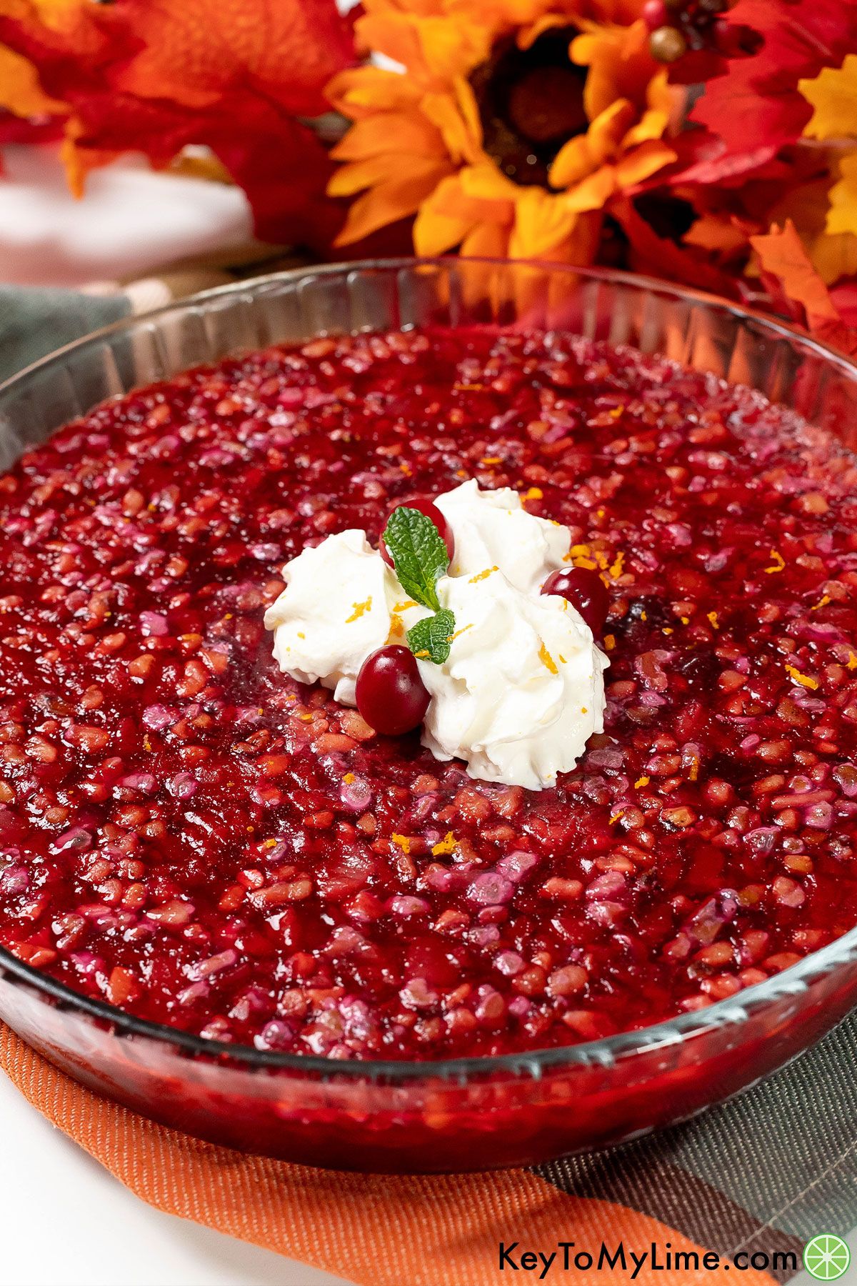 A close up image of cranberry jello salad inside a large glass bowl on top of a multicolored napkin.