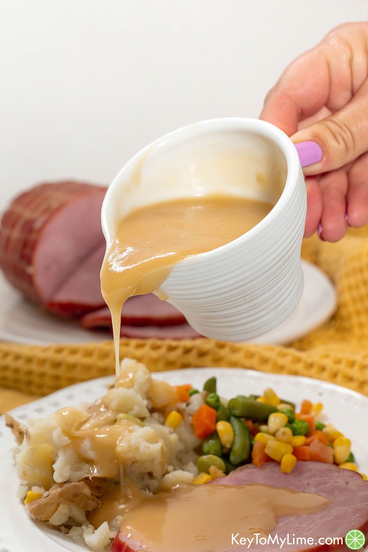 Pouring gravy on top of a slice of ham.