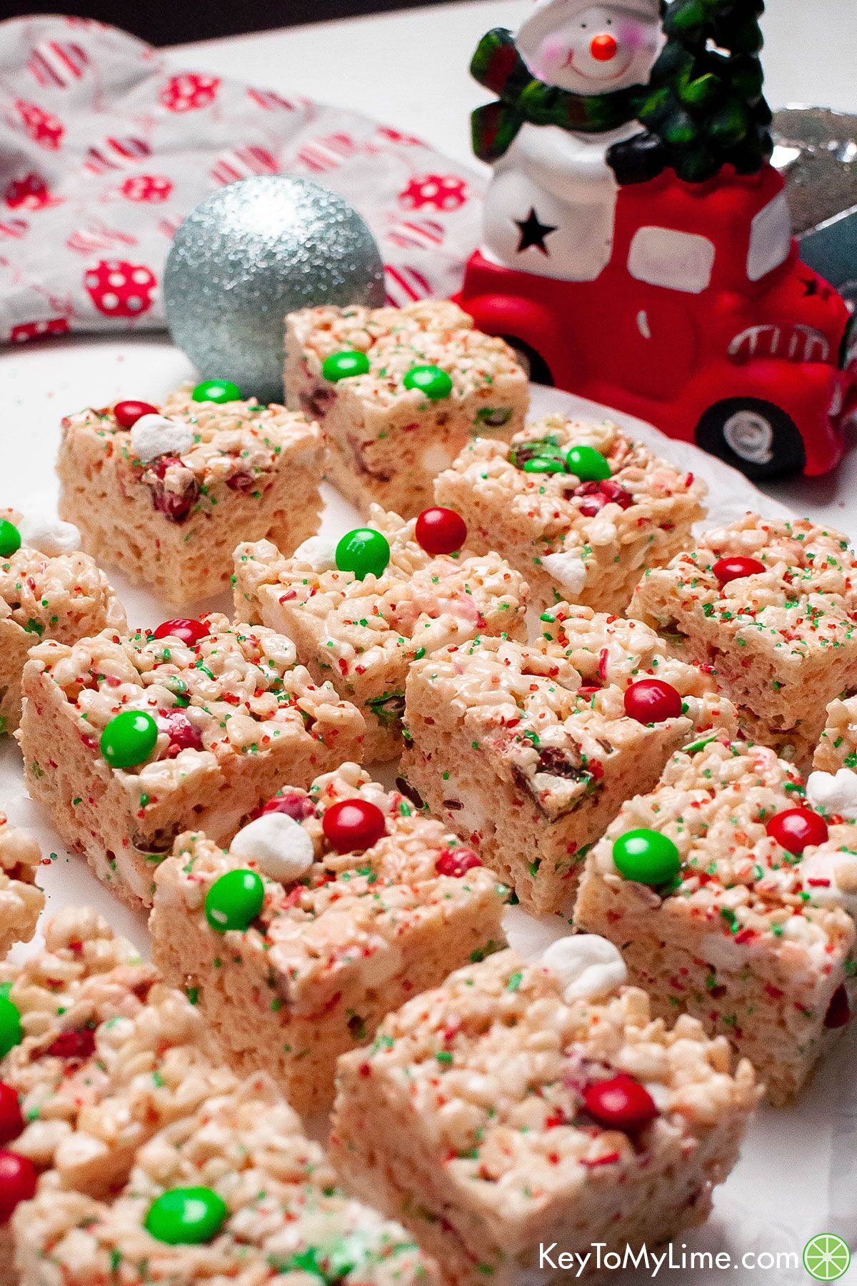 An image of krispie squares on top of a parchment paper with Christmas props in the background.