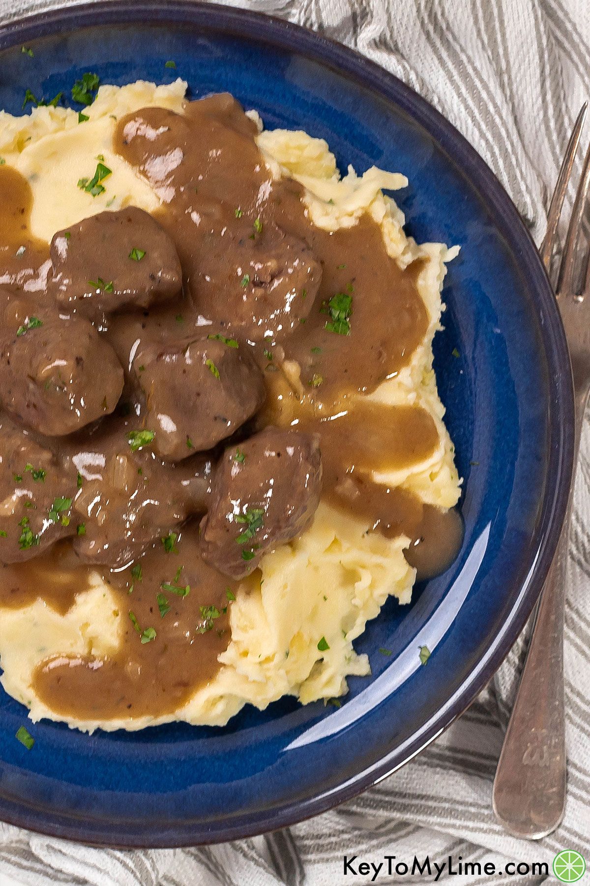 A close up image showing the texture of beef tips and gravy on a plate of mashed potatoes.