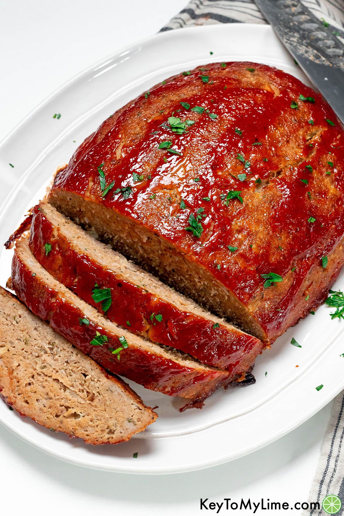 An overhead image of a fully cooked chicken meatloaf with multiple splices cut served on a white platter.