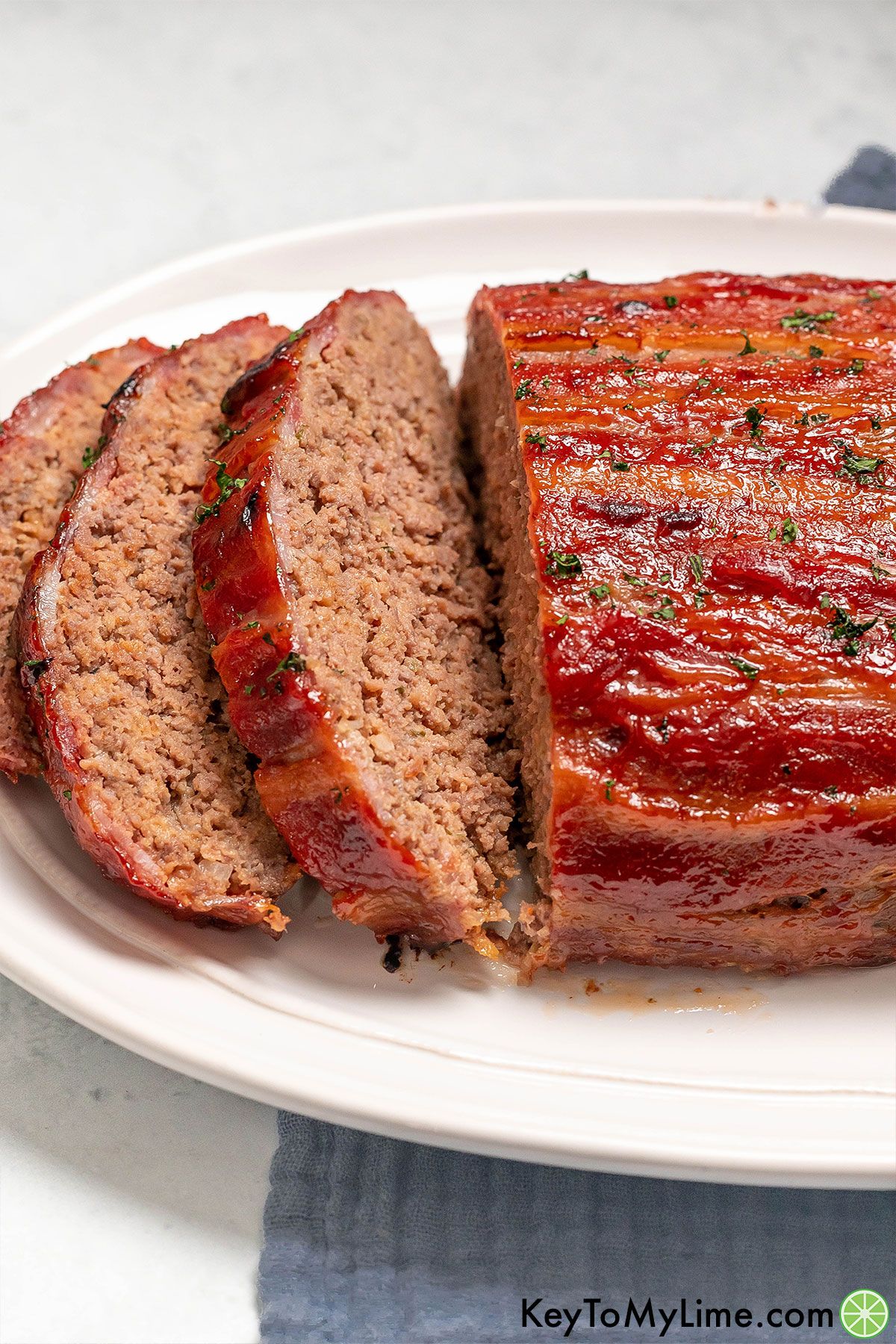 A delicious partially cut meatloaf on a large white platter.