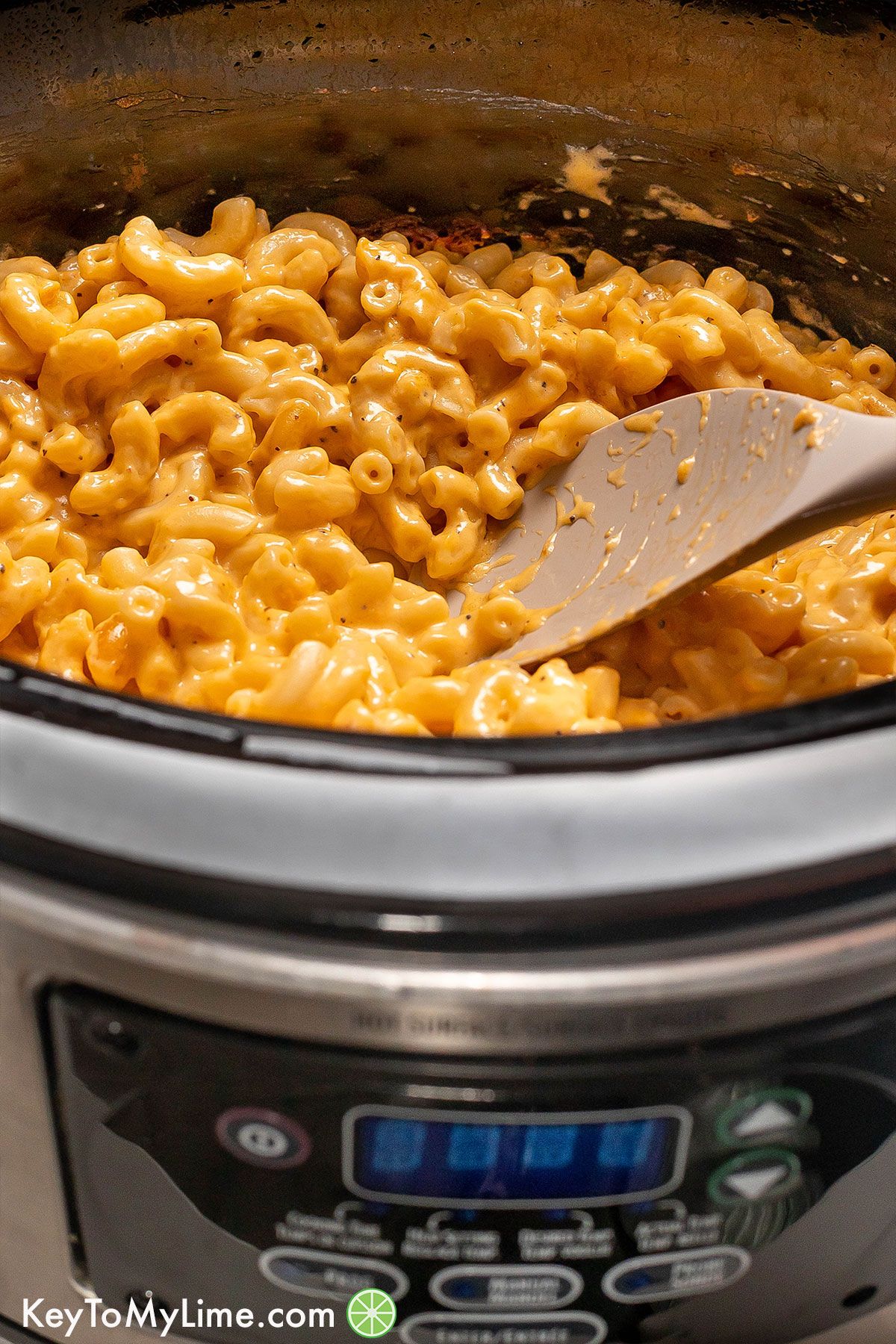 A side shot of mac and cheese on a serving spoon inside of a crockpot.