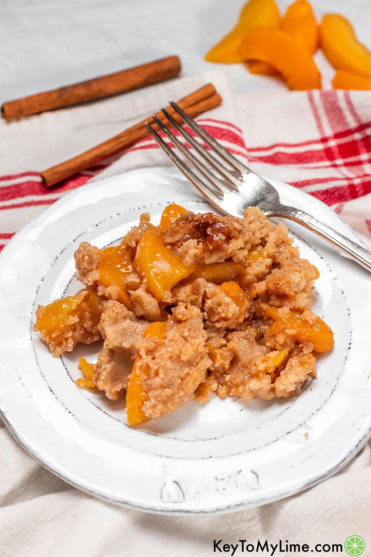 A scoop of peach crumble next to a fork on a white plate.