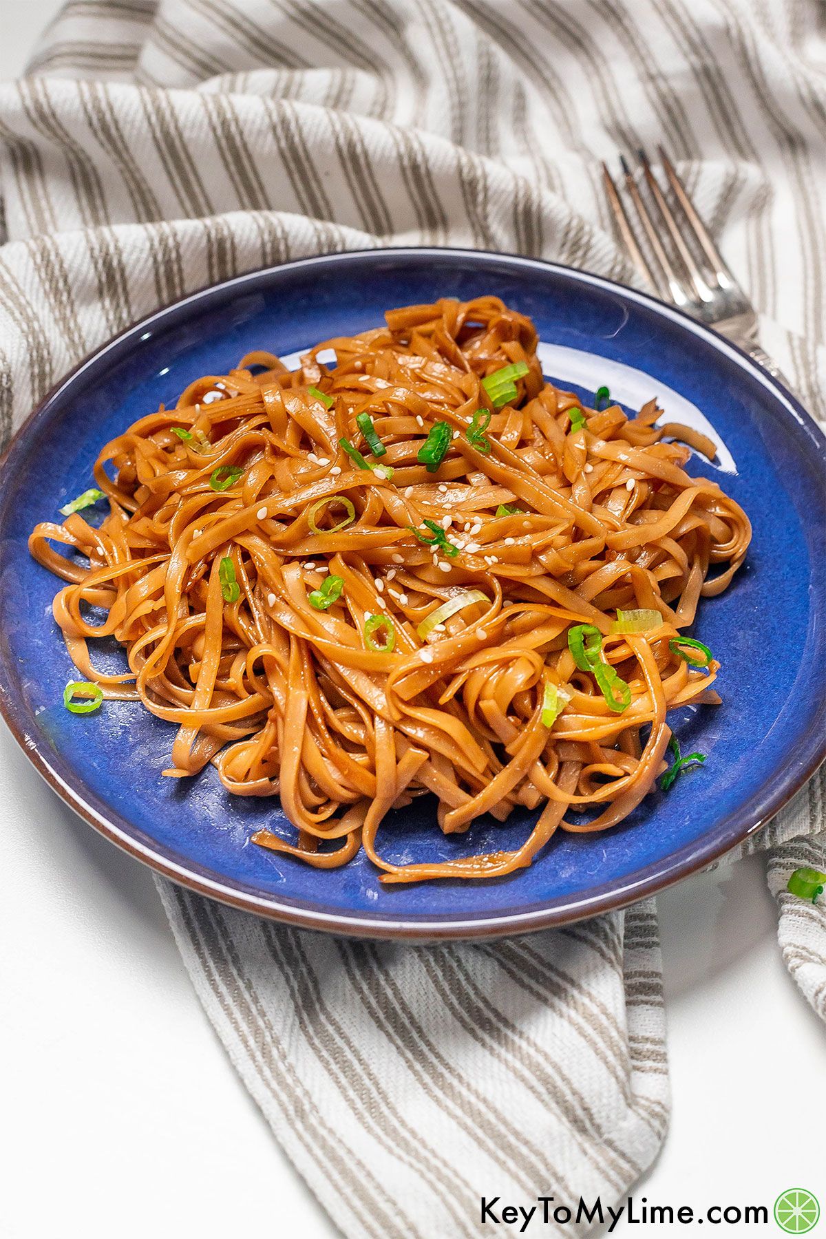 A plate of noodles coated in teriyaki sauce on top of a napkin.