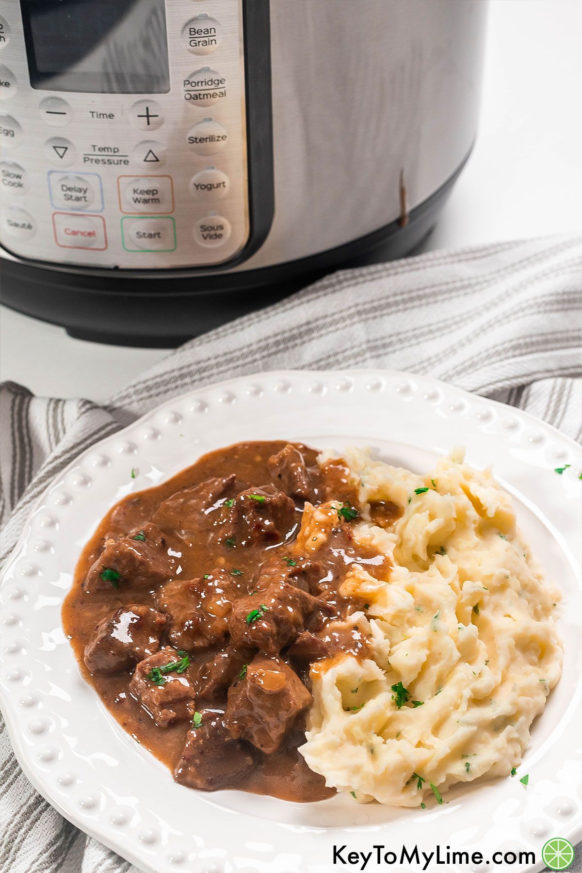 Fall apart beef tips in a flavorful gravy on a white plate next to an Instant Pot.
