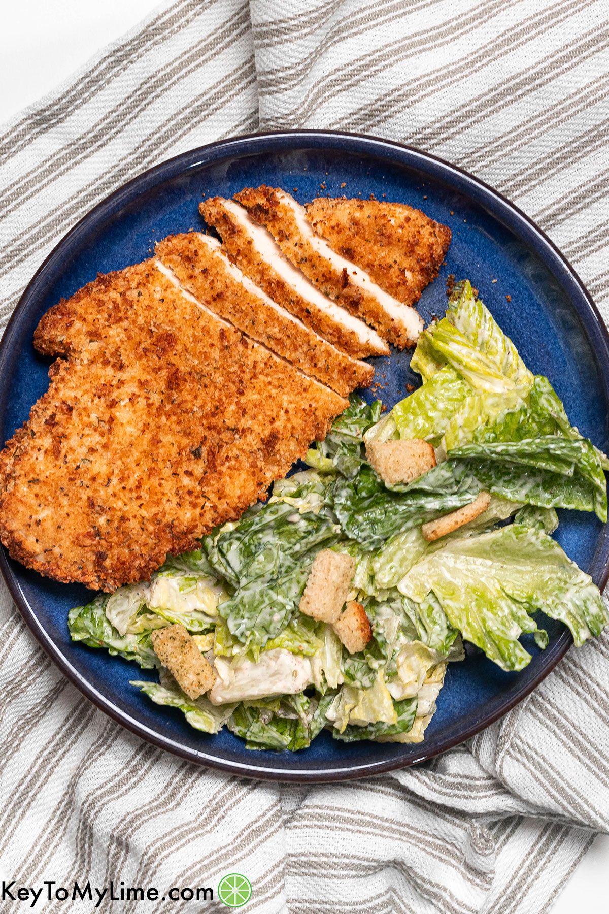 An overhead shot of a sliced chicken cutlet next to a caesar salad.
