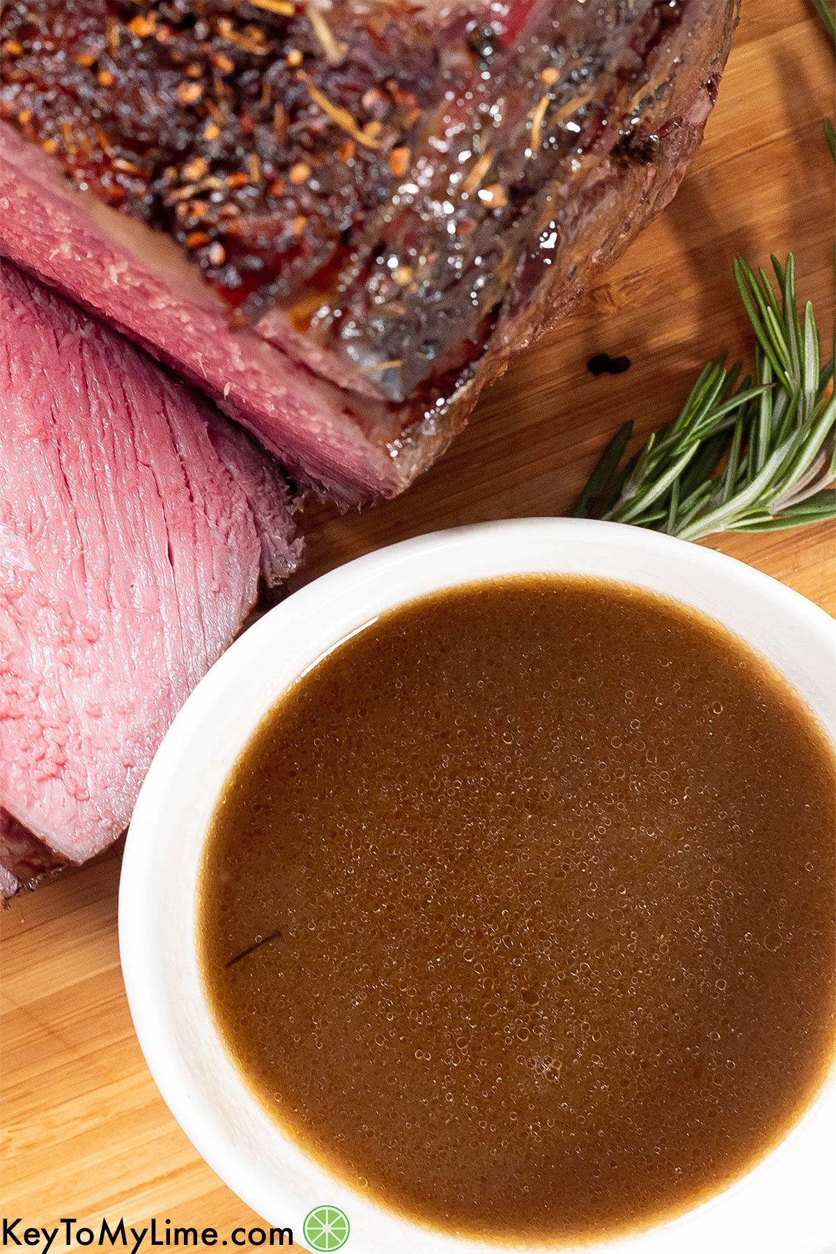 An overhead shot of a bowl of au jus next to a slice of roast.