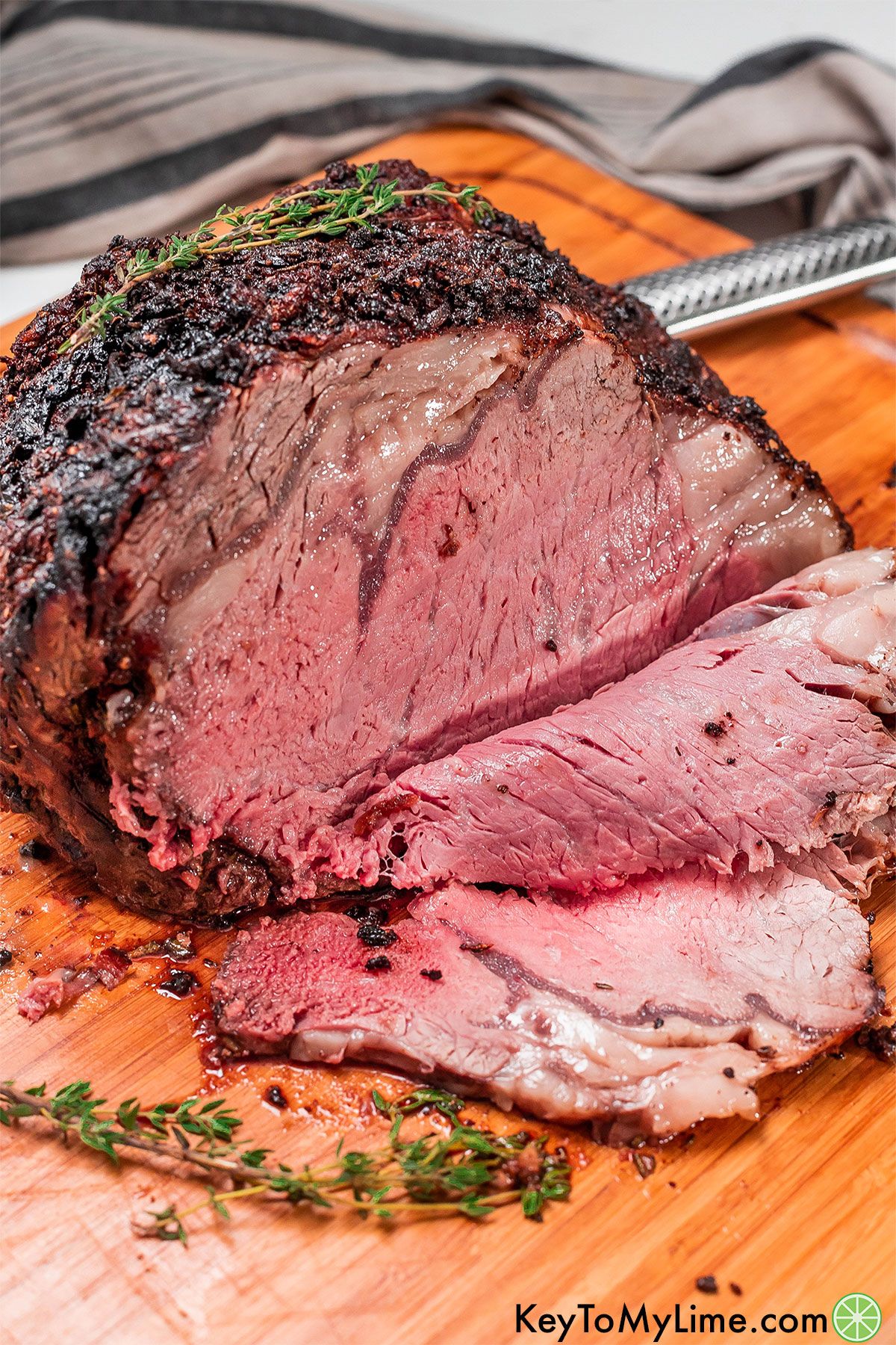 A partially cut prime rib roast with multiple thin slices on a wood cutting board.