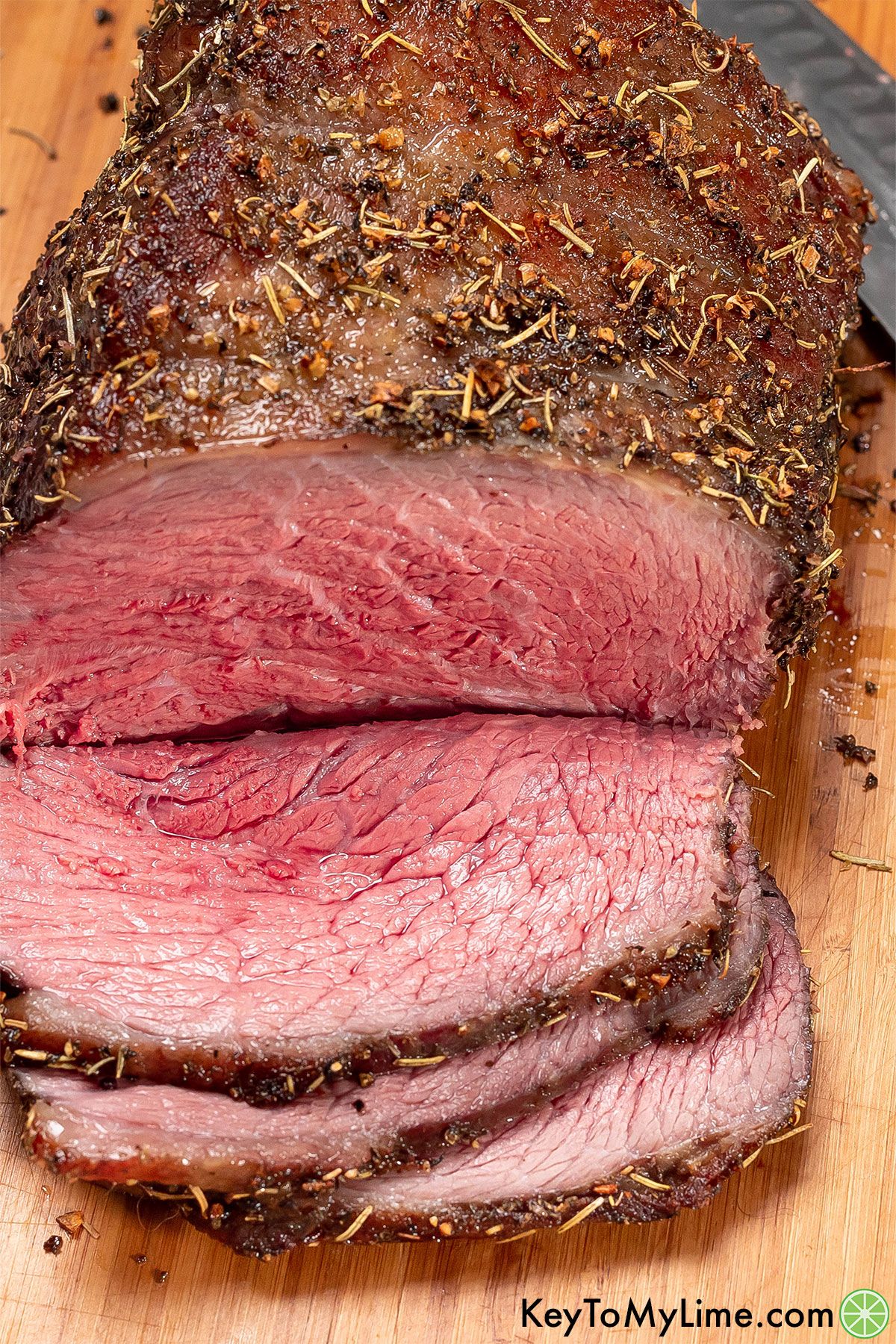 A cooked roast covered in a beautiful rub with a few slices cut on a cutting board showing the juicy tender slices.