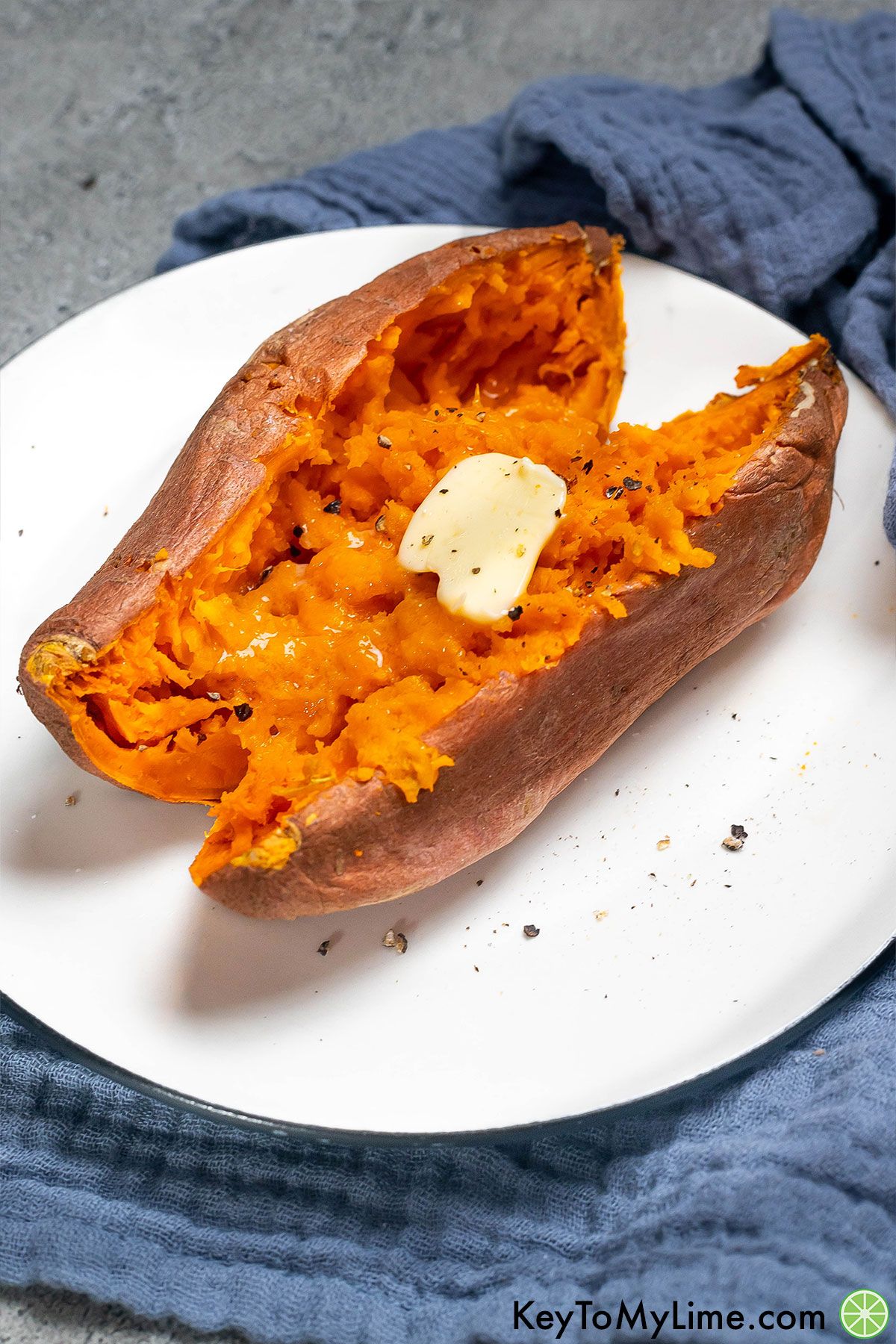 A fully microwaved sweet potato garnished with butter served on a plate.