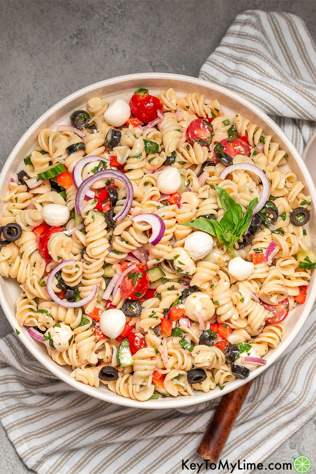 An image of pasta salad inside a large serving bowl on top of a striped napkin.