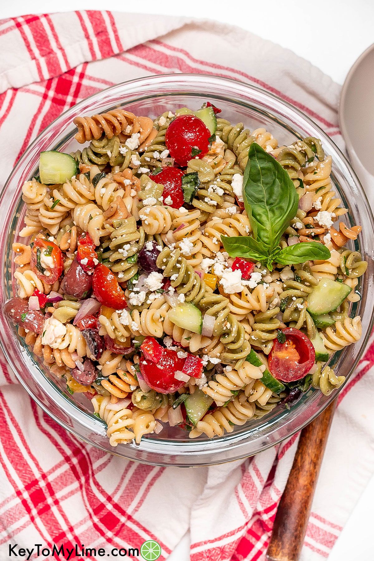 An overhead image of a large bowl filled with freshly made rotini pasta salad on top of a red napkin.