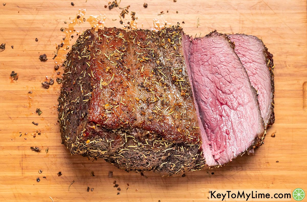 A bottom round roast with a slice of beef on top of a wood cutting board next to a knife.