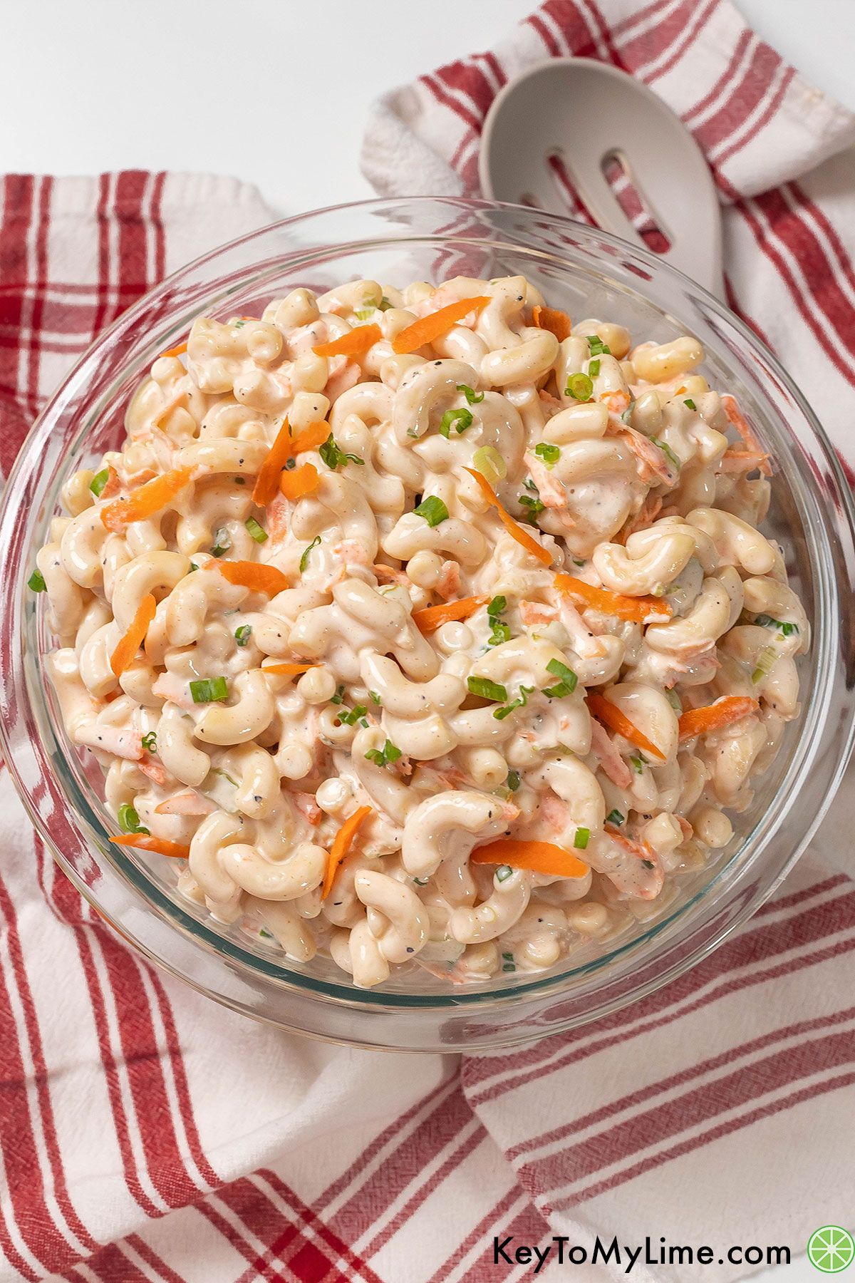 A large mixing bowl full of macaroni salad garnished with fresh green onion.