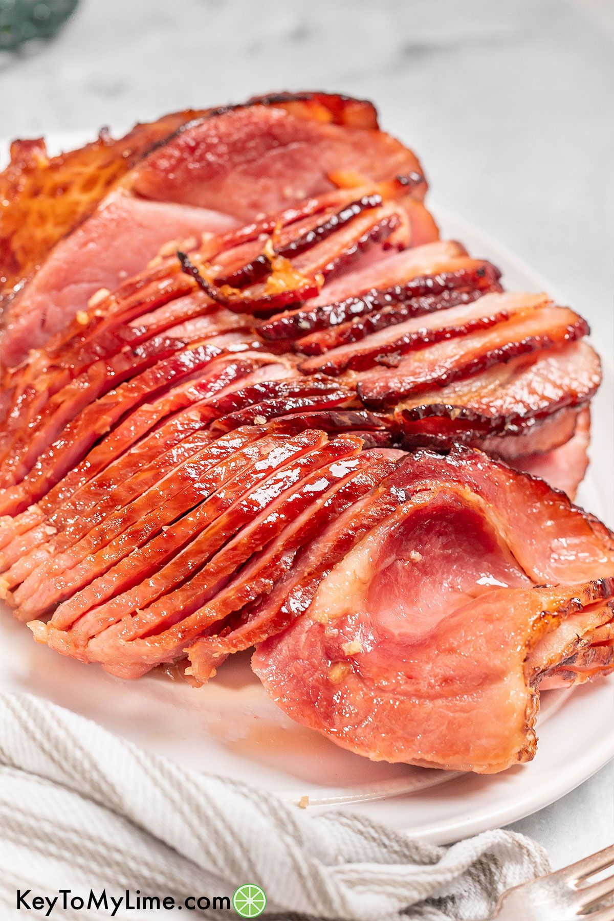 Rows of thinly sliced ham on a white dish showing the broiled crispy edges.