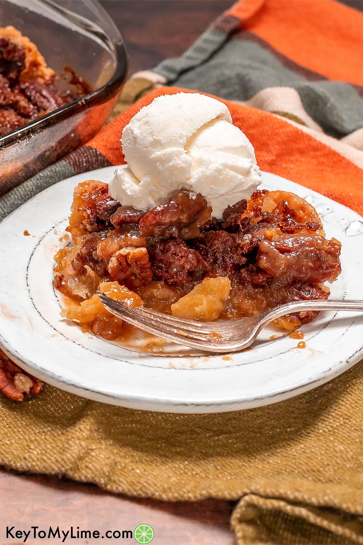 A side image of a serving of pecan cobbler topped with a scoop of ice cream on top of a white plate.